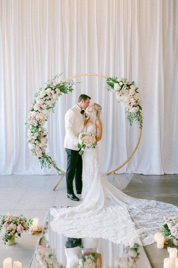 Bride and groom kissing in front of circle arch and florals with candles at Aria ballroom wedding