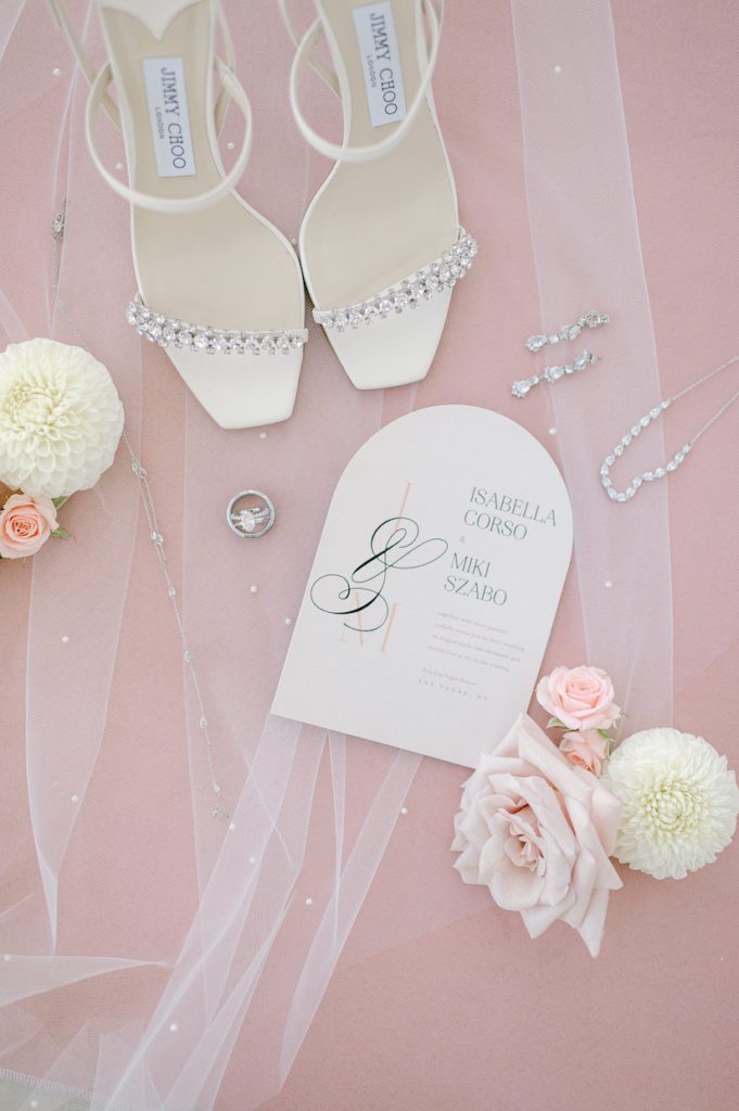 Wedding flat lay with invitation ring shoes earrings and pink blush backdrop