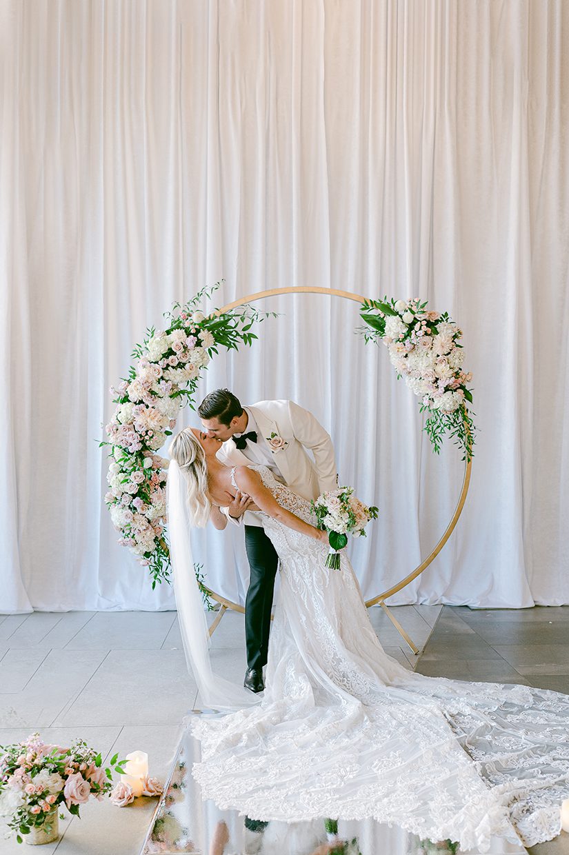 groom dipping bride in front of floral arch at aria wedding in las vegas