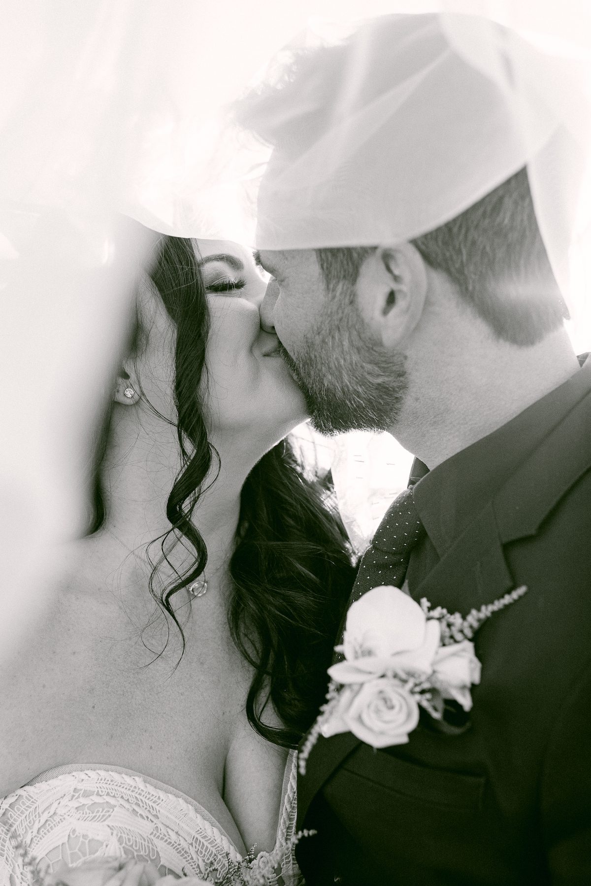 bride and groom sharing a kiss draped in brides veil with in black and white