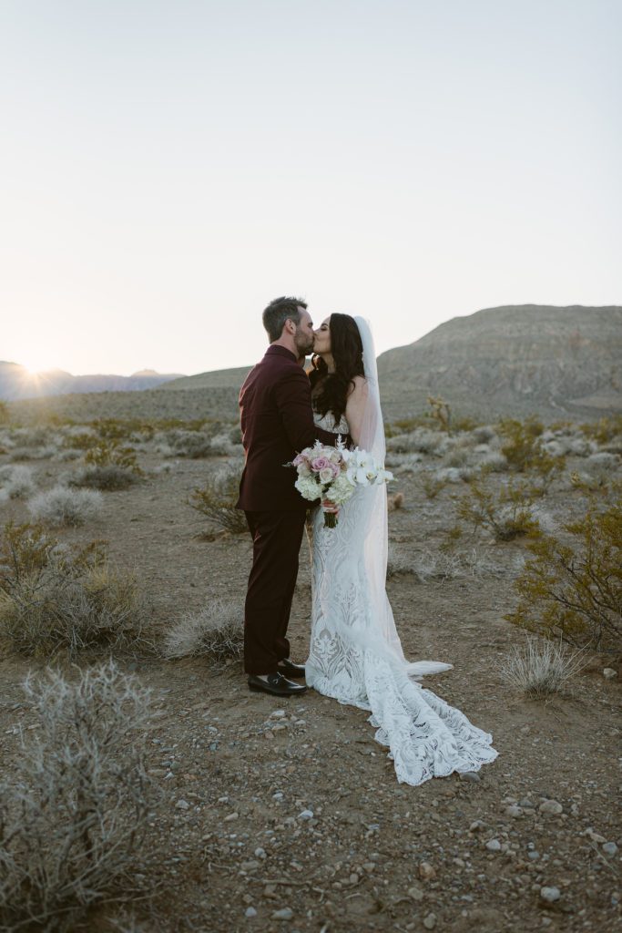 bride and groom sharing a kiss bride wearing long veil and lace wedding gown with soft light backlighting couple in red rock canyon