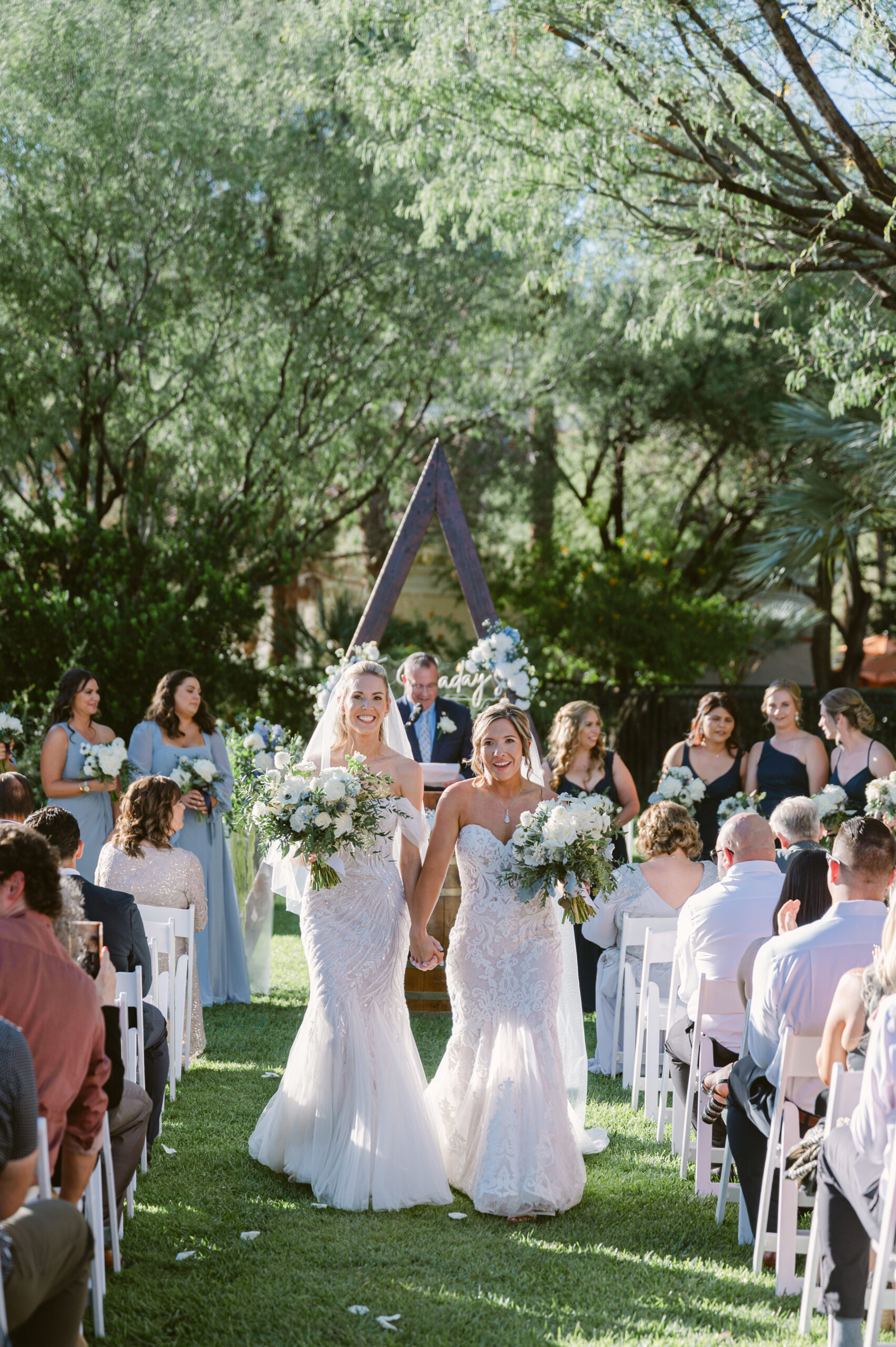Two Gay Brides walking down the aisle in greenery triangle arch las vegas photography